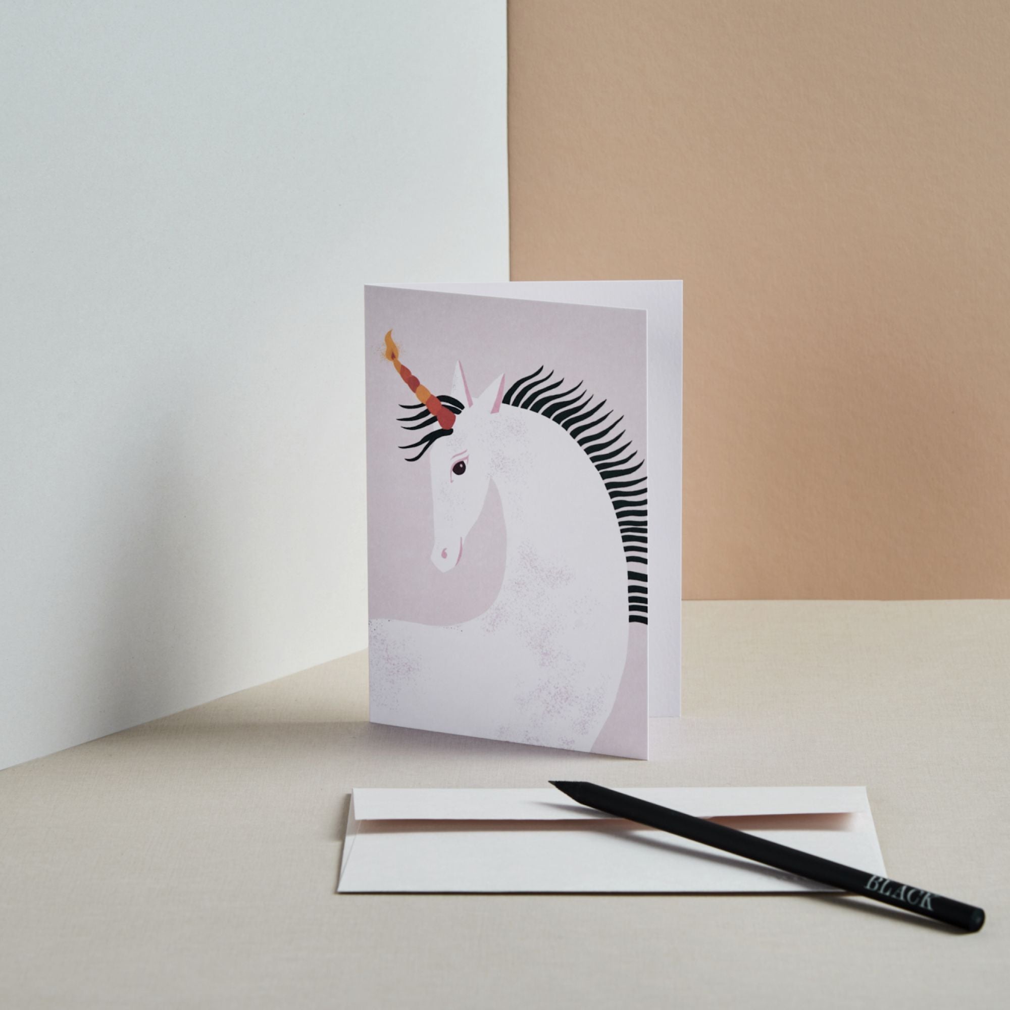 Grußkarte mit stilisiertem Einhorn auf hellviolettem Hintergrund, weißem Umschlag und schwarzem Bleistift