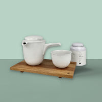 Minimalistisches weißes Keramik-Teeset mit seitlichem Henkel, Tasse ohne Henkel und Deckelbehälter auf Holztablett.