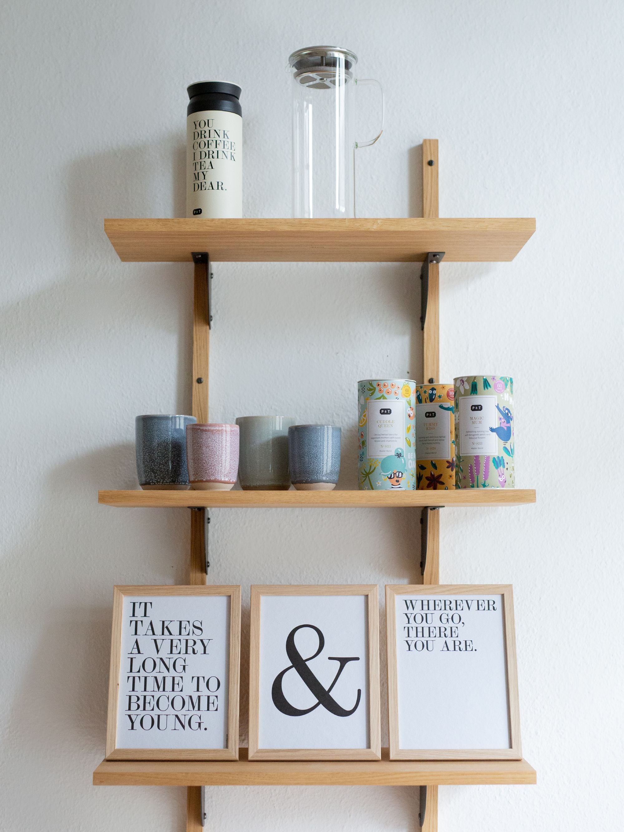 Minimalistisches Holzregal an weißer Wand mit Thermobecher, French Press, Keramiktassen und Paper & Tea Teedosen.