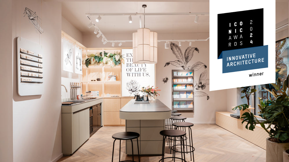 Moderner Küchenbereich mit Insel, schwarzen Hockern, Menü mit Cold Brew und Matcha, botanischer Wandkunst.