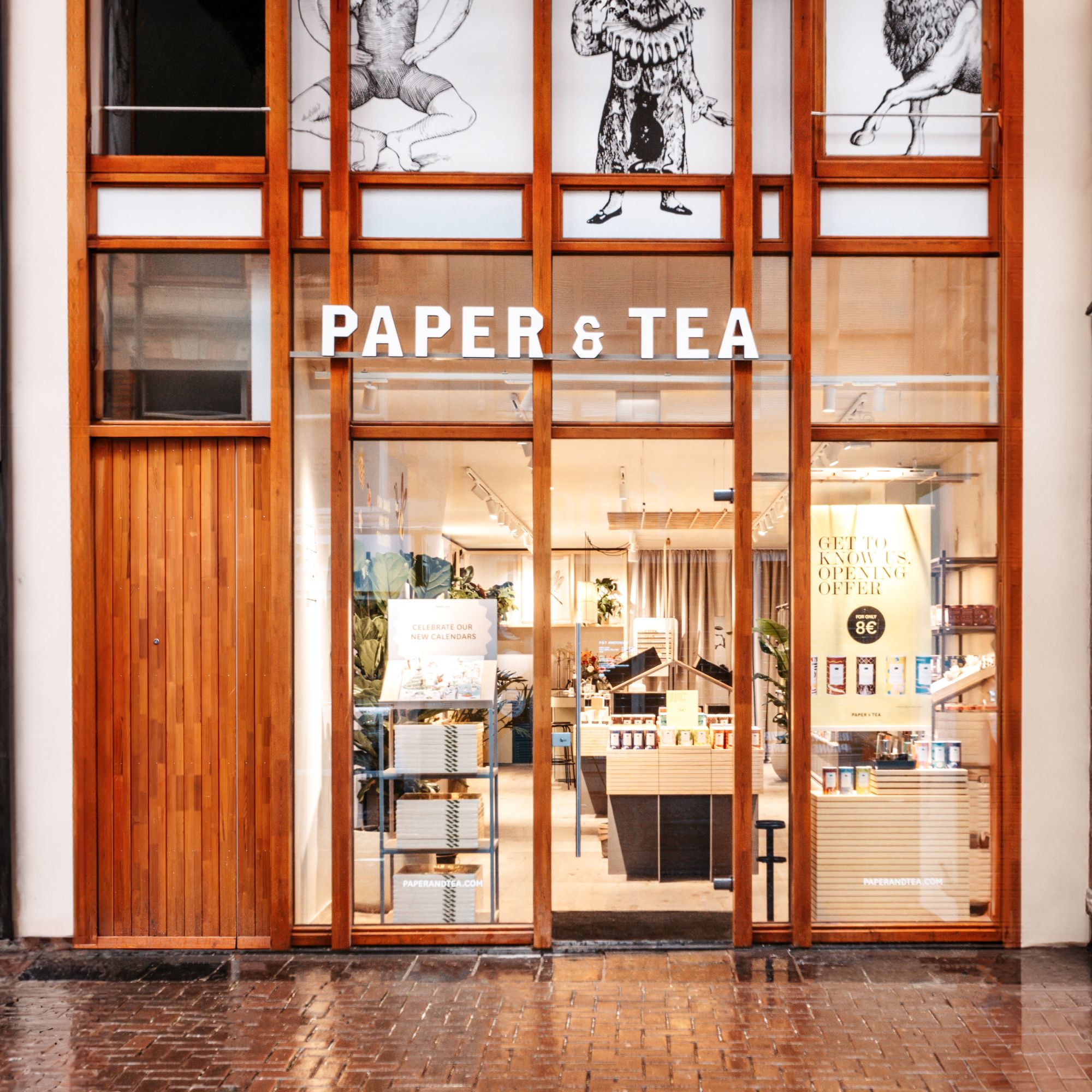 Einladender PAPER & TEA Laden mit großen Fenstern, Holzrahmen, Kalendern für 8 €, Illustrationen und Pflanzen.